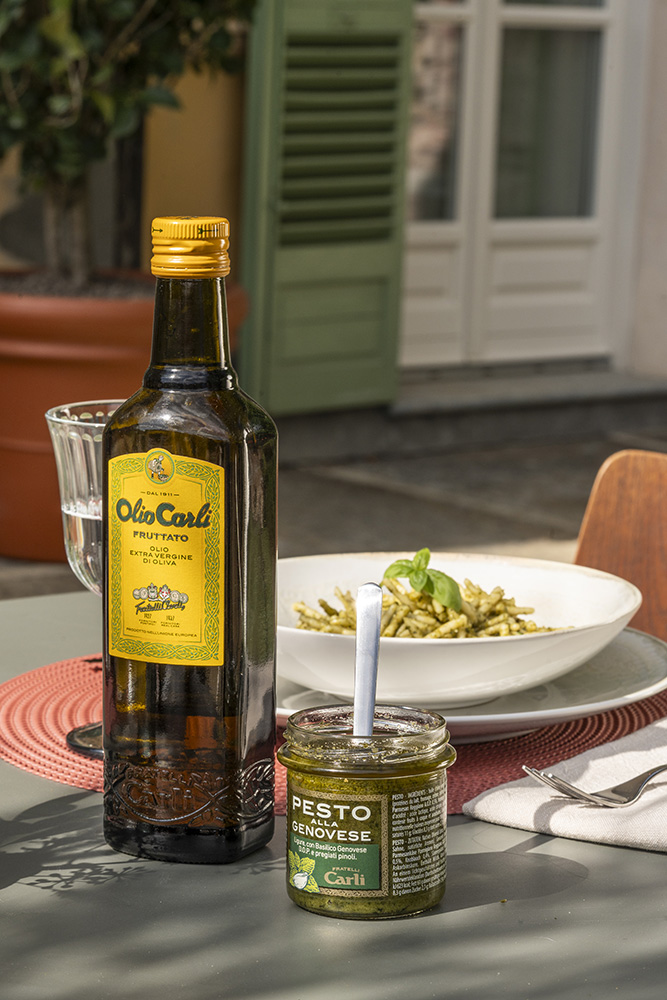 Bottiglia di Olio Evo Fruttato, a fianco ad un vasetto di Pesto alla Genovese su una tavola